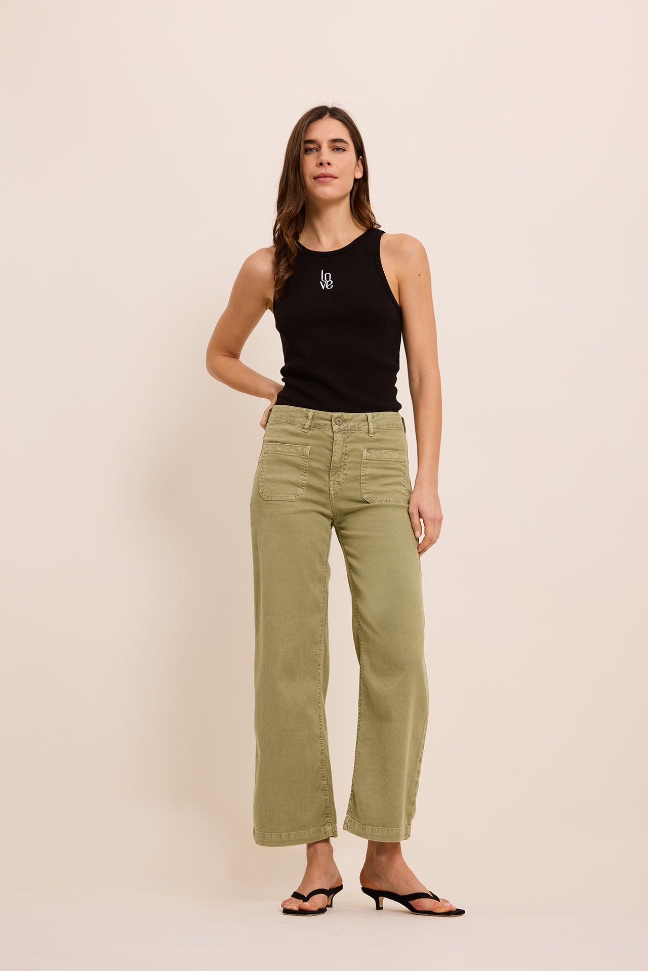 Woman wearing a black tank top and green pants against a beige background