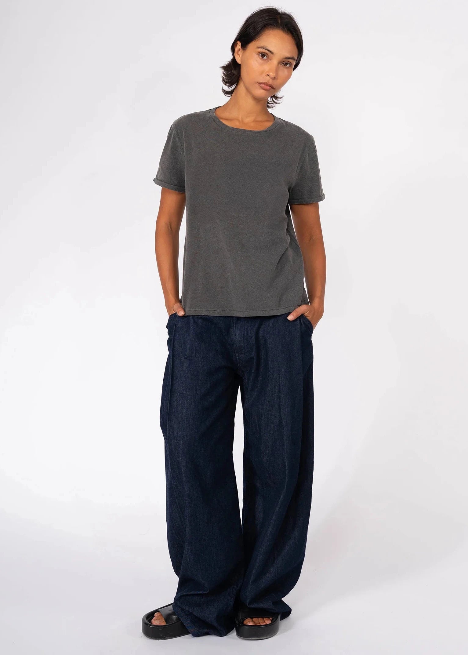 Woman wearing a gray t-shirt and dark blue wide-leg pants on a white background